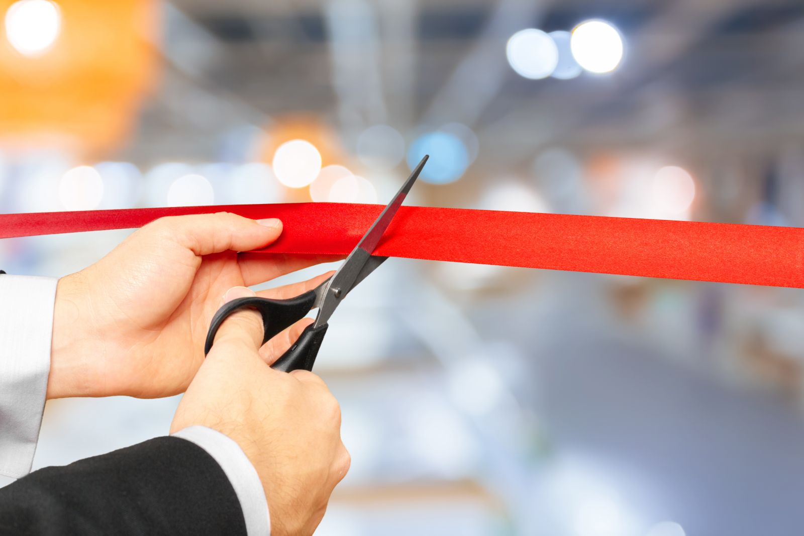 Hands cutting a red ribbon at a grand opening