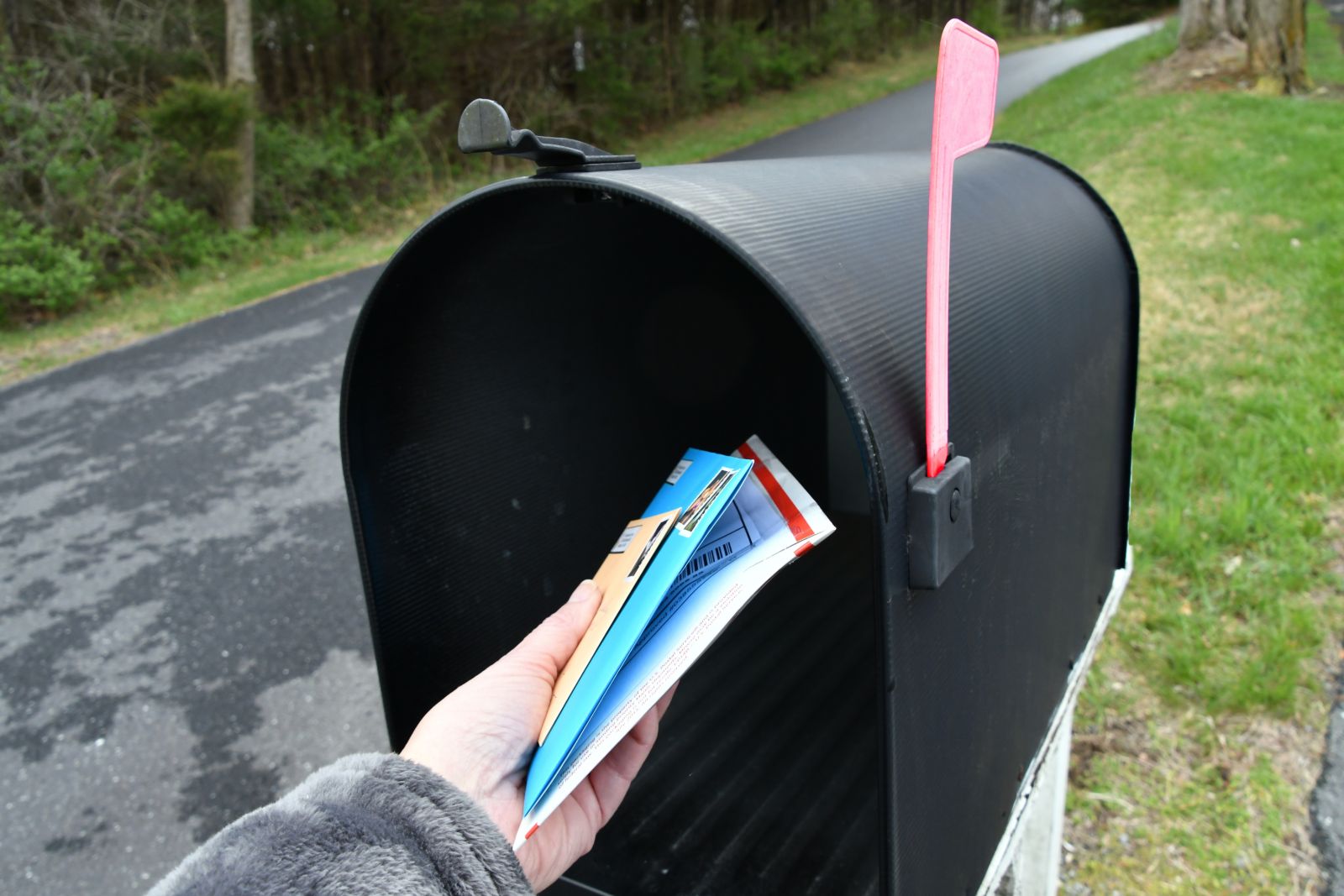 Hand placing mail in a black mailbox